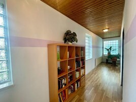 A hallway with a wooden bookshelf, a ceiling with wooden slats, and a window with a view of trees.