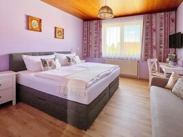 A bedroom with a large bed, a desk, and a chair. There are two framed pictures on the wall.