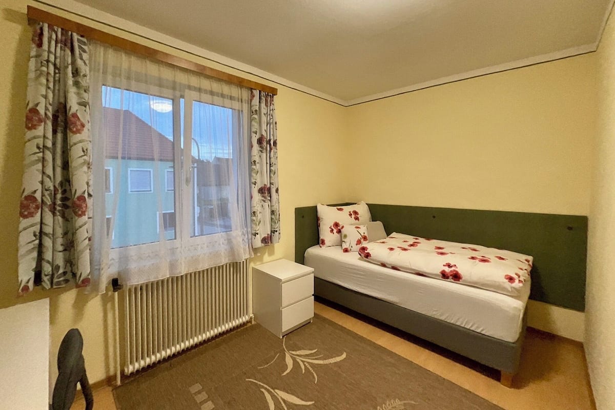 Une chambre avec un lit simple, un radiateur, une table de chevet et une chaise.
