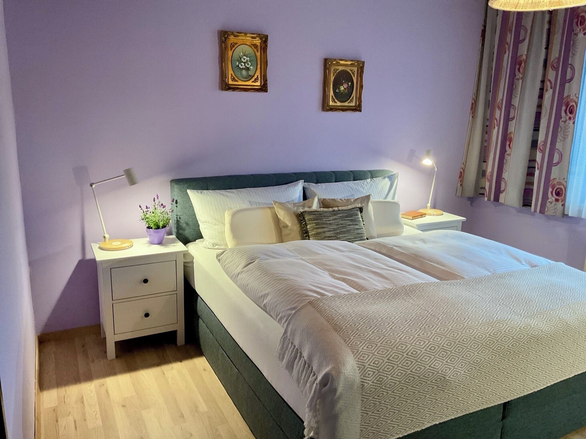 A neatly arranged bedroom with a bed, bedside tables, a lamp, and two framed pictures on the wall.