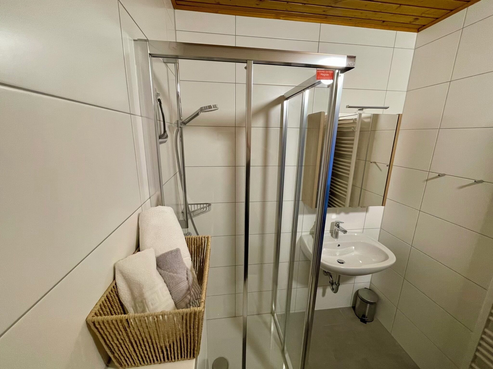 Un baño moderno con ducha envuelta en vidrio, lavabo y una cesta de mimbre con toallas.