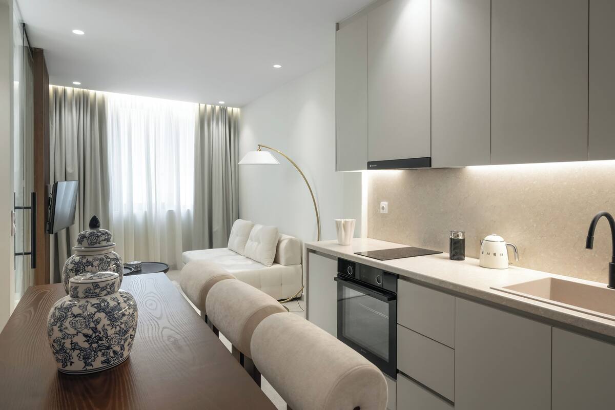 A modern kitchen with a built-in oven, a sink, and a dining area with a sofa and a table.