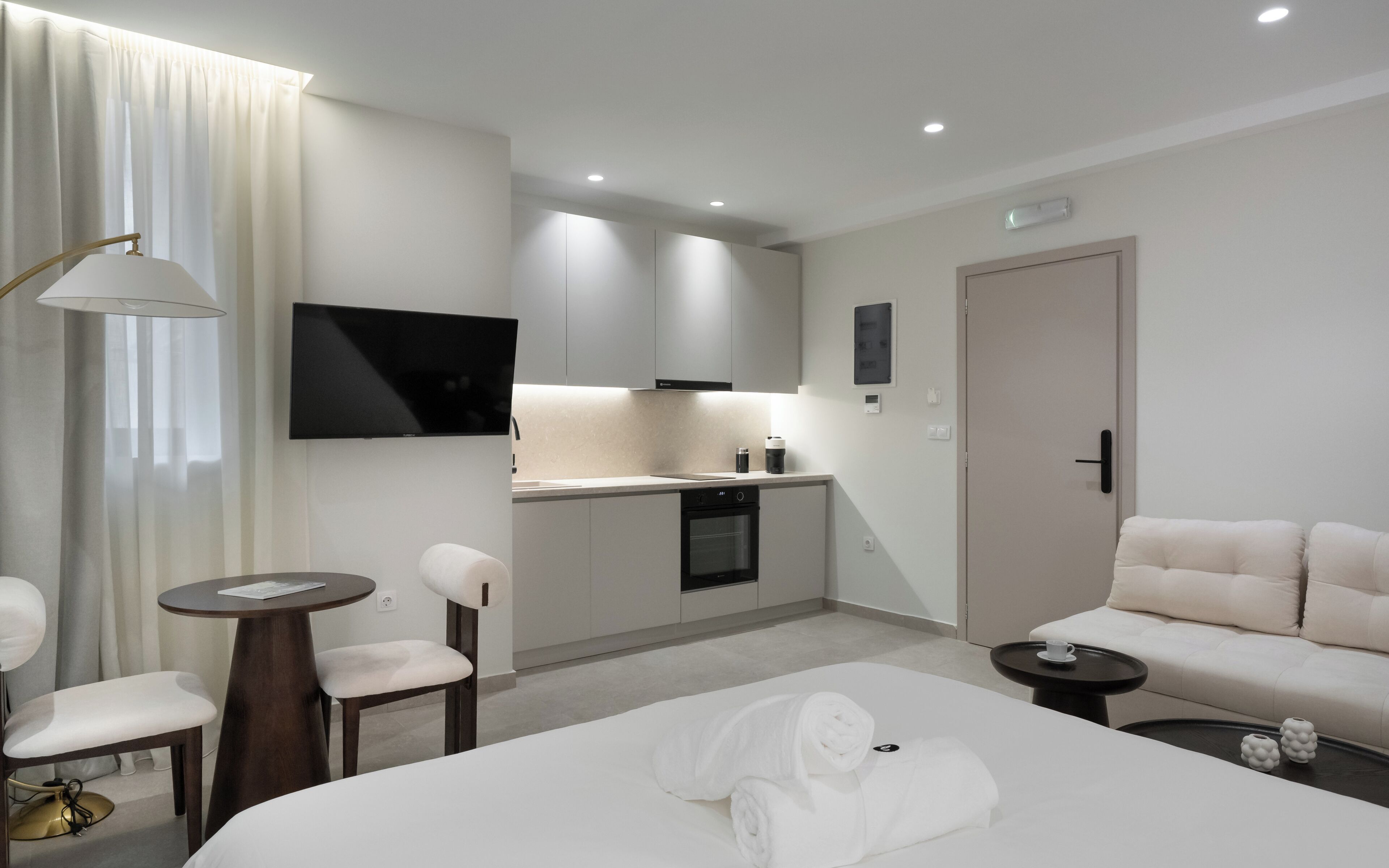 A modern hotel room with a bed, a desk, a chair, a sofa, a small table, and a television.