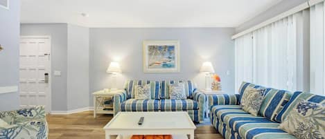 A living room with striped sofas, a white coffee table, and a painting on the wall.