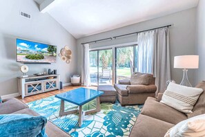 Una sala de estar moderna con televisor, sofá, mesa de centro y vistas al exterior.