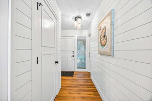 Un pasillo con paneles blancos en las paredes, suelo de madera y una puerta que da a una habitación.