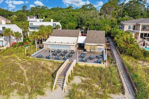 A beachfront property with a covered parking area, a small building with a sign, and a pathway leading to the beach.