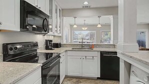 Cucina con mobili bianchi, un forno a microonde nero, un fornello, una lavastoviglie e lampade a sospensione.