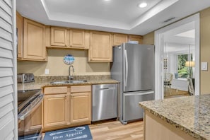 A kitchen with wooden cabinets, stainless steel appliances, granite countertops, and a clock on the wall.