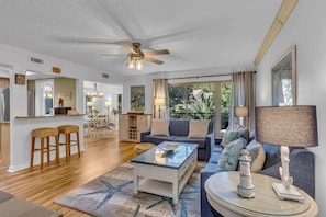 A spacious living area with a ceiling fan, a sofa, a coffee table, and a dining area with a chandelier.