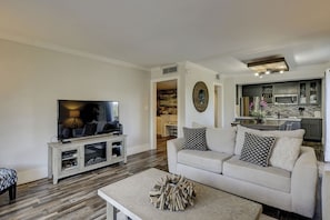 A living room with a TV, sofa, coffee table, and a kitchen in the background.