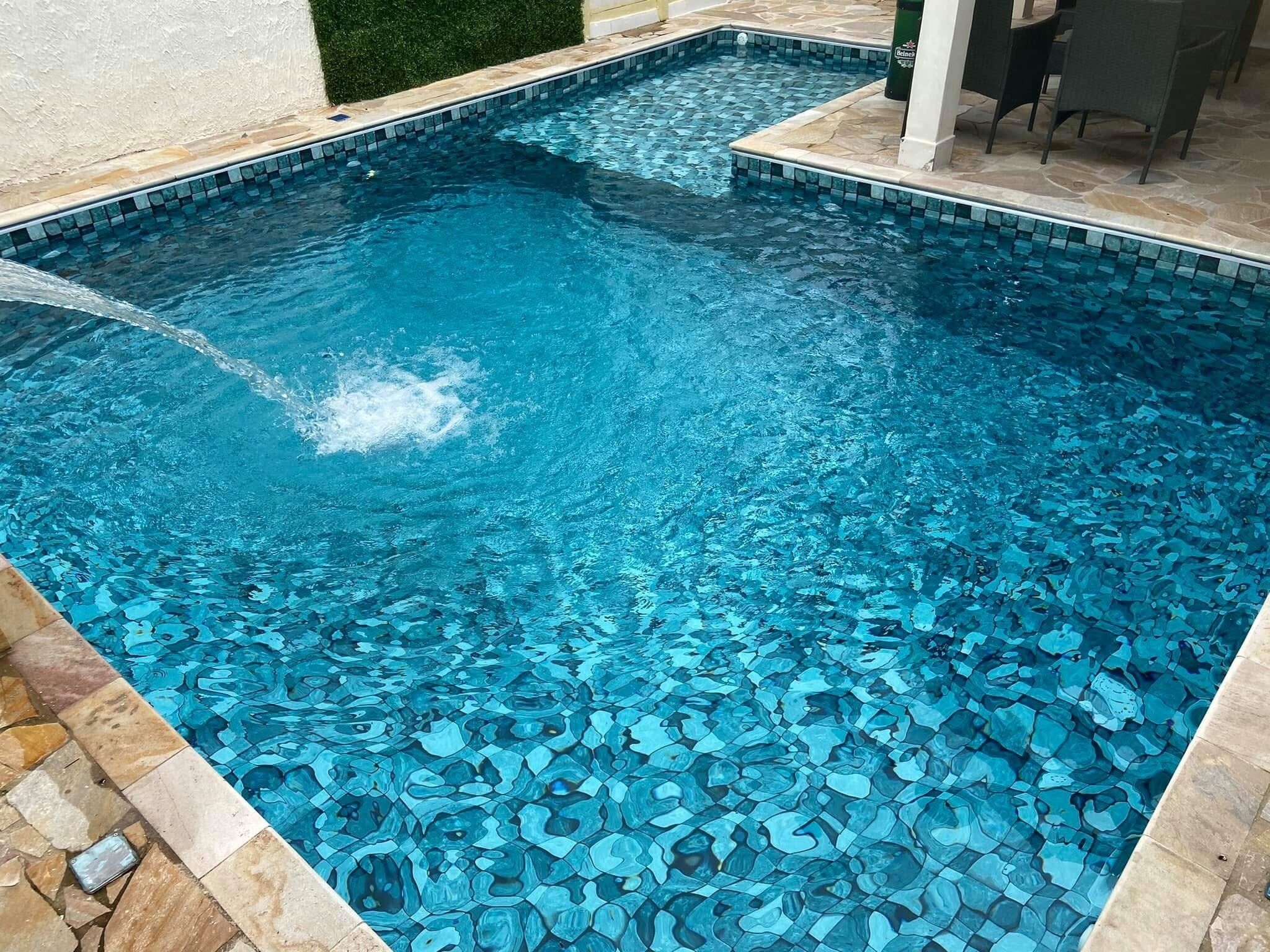 A swimming pool with a mosaic tile design, surrounded by stone tiles and a small grassy area.