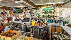Un bar con temática tropical, incluyendo un letrero que dice 'POOL BAR JIM'S Tropical & Exotic Frozen Drinks'.