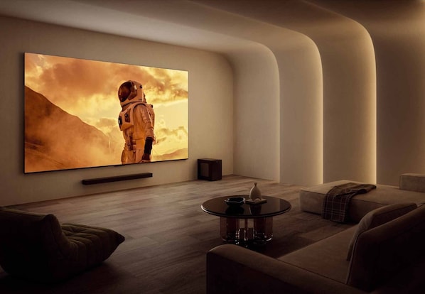 Una sala de estar moderna con una gran televisión de pantalla plana montada en la pared, una mesa de centro redonda y un sofá.