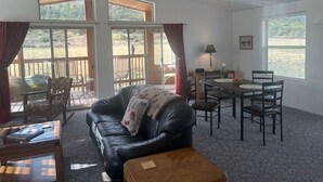 A spacious living room with a leather sofa, a dining table with chairs, and large windows offering a view of the outdoors. - Great Space for Relaxing, Roomy House. Trailer Parking Plentiful, 3 Acres (South Fork)
