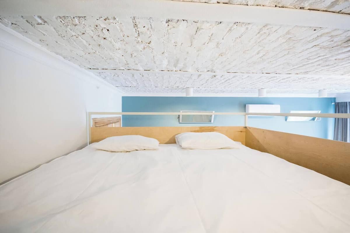 A single bed with a wooden headboard, white bedding, and a view of the sky through a window.