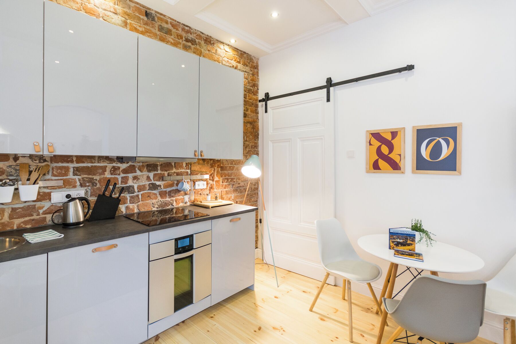 Una cocina moderna con armarios blancos, una pared de ladrillo decorativa y un comedor con una mesa blanca y dos sillas.