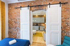 A room with a brick wall, a bed with a blue cover, and a kitchen visible through an open door. - AS HOME Szewska (Wrocław)