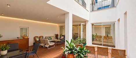 A modern apartment with a wooden deck, indoor seating area, and a balcony with wicker furniture.