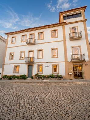 Un hôtel à la façade classique, doté de nombreux balcons, situé sur une rue pavée.