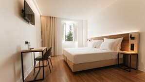 Une chambre d’hôtel avec un lit, un bureau, une chaise, une télévision et une fenêtre avec des rideaux.