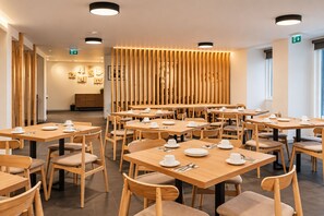 Un espace repas moderne avec des tables et des chaises en bois, agrémenté de vaisselle blanche.
