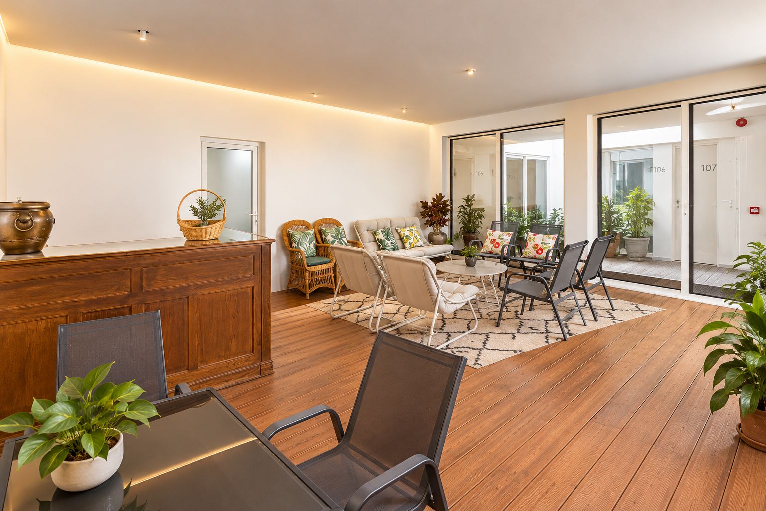 A modern interior with a wooden reception desk, wicker chairs, a round table, and potted plants.