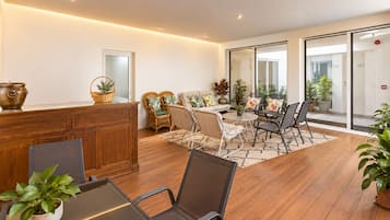 A modern interior with a wooden reception desk, wicker chairs, a round table, and potted plants.