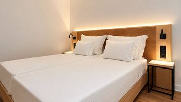 A modern hotel room with a large bed, white linens, a wooden headboard, bedside lamps, and a nightstand.