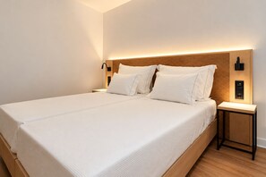 Una habitación de hotel moderna con una cama grande, ropa de cama blanca, cabecera de madera, lámparas de noche y una mesita.