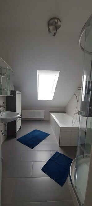 A modern bathroom with a skylight, a bathtub, a shower, and a sink. - Holiday Apartment 'Merkurblick Loffenau' with Private Terrace and Wi-Fi (Loffenau)