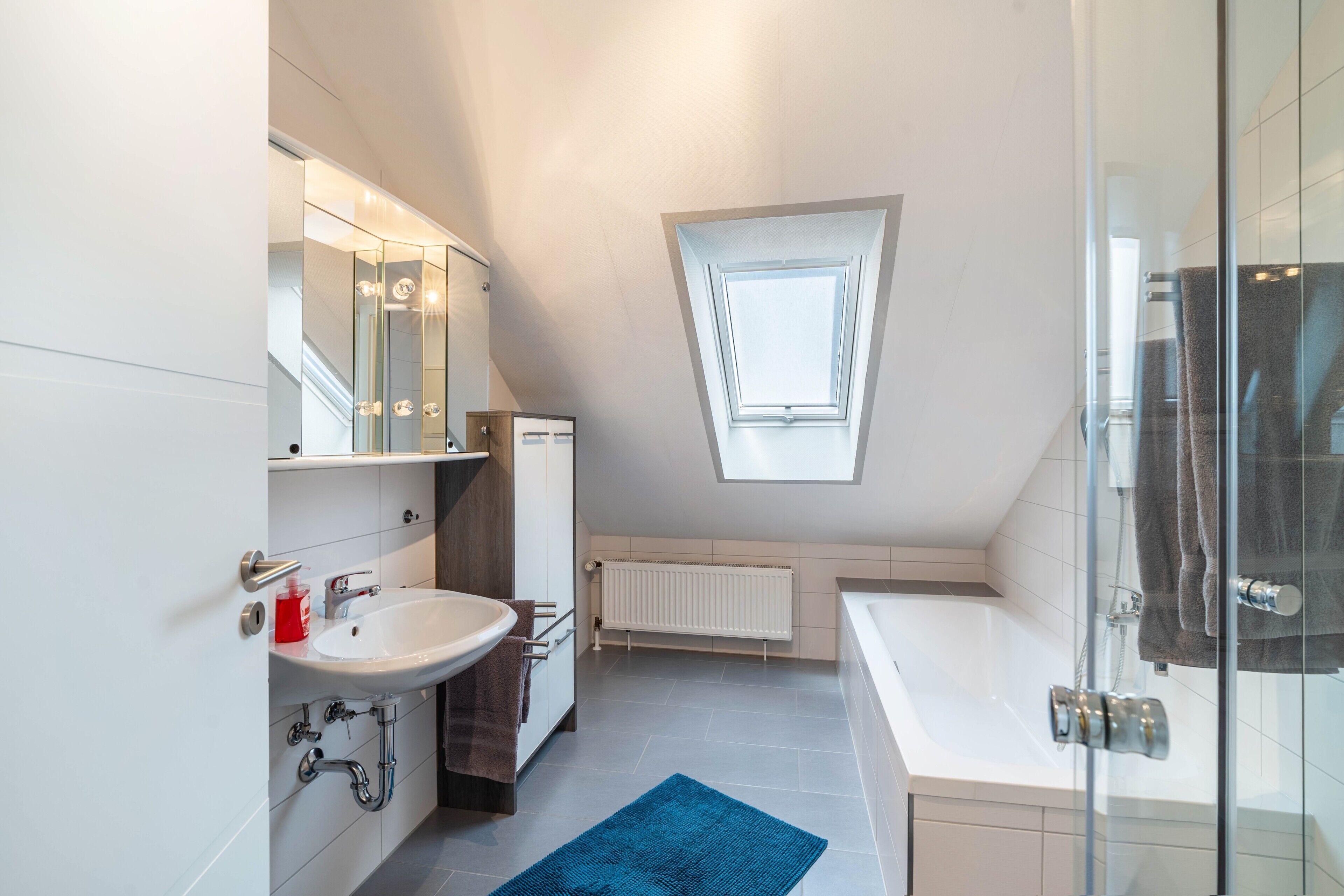 A modern bathroom with a skylight, a bathtub, and a shower area.