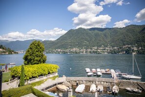 A lakeside view with boats docked, a tree, and mountains in the background. - Cernobbio in Riva. Lake views, Steps from Lake. (Cernobbio)