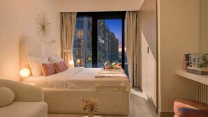 Quarto de hotel moderno com uma cama grande, área de estar e vista para a cidade pela janela.