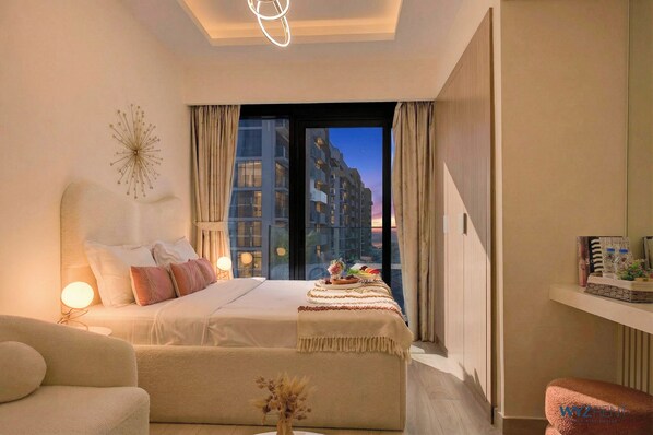 A modern hotel room with a large bed, a sitting area, and a view of the cityscape through the window.