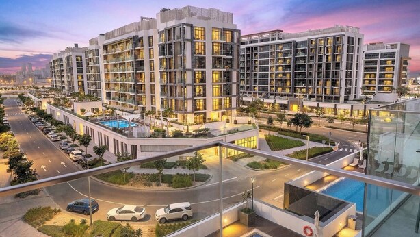 Um moderno complexo hoteleiro com vários edifícios altos, piscina e área externa bem cuidada, com árvores e uma estrada.