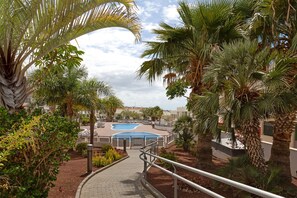 Ein Weg führt zu einem Pool, der von Palmen umgeben ist, unter einem klaren Himmel.