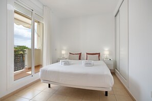 Ein Schlafzimmer mit einem Bett, zwei Nachttischen, einem Fenster mit Vorhängen und Blick nach draußen.