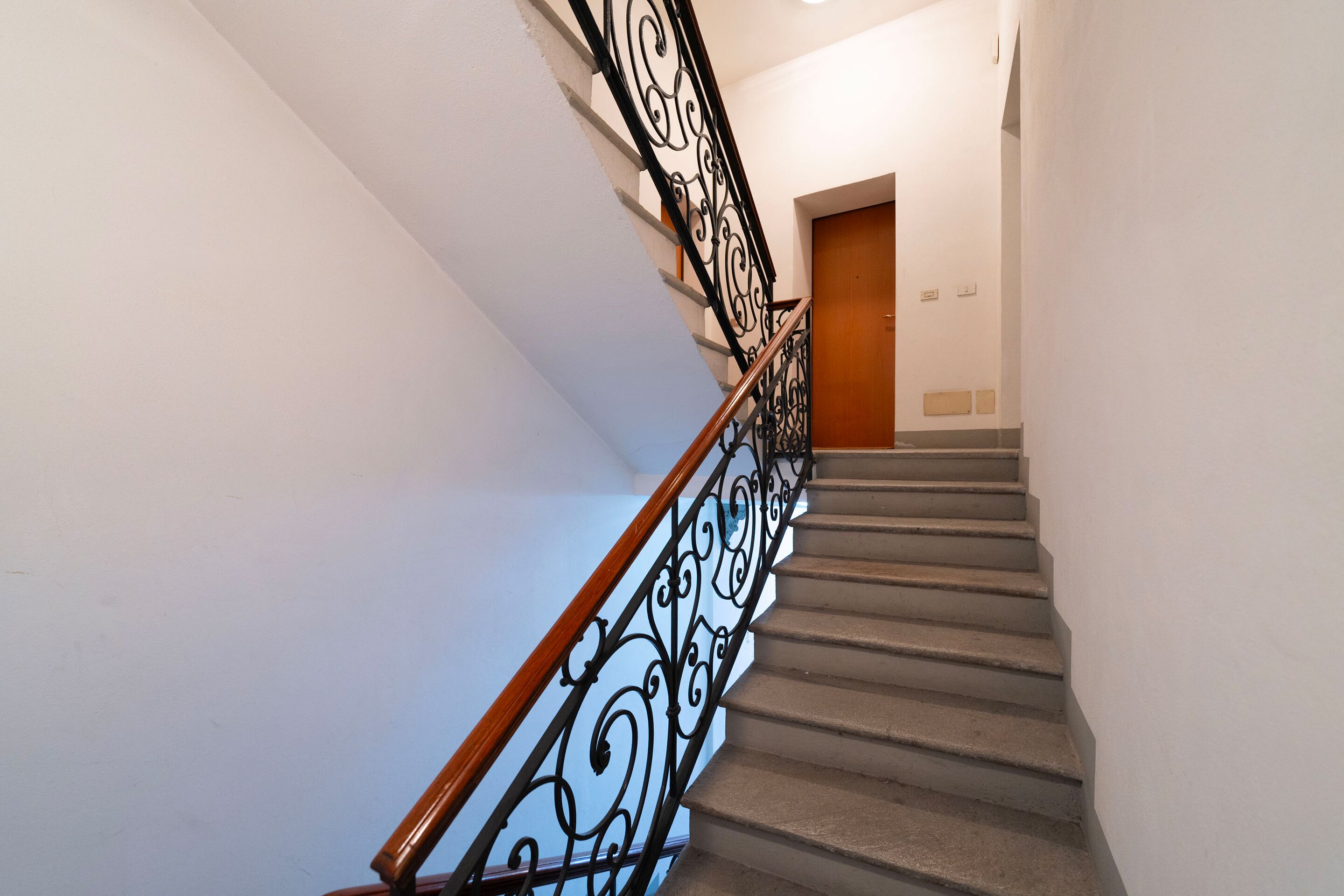 A staircase with a wooden handrail and black metal balusters.