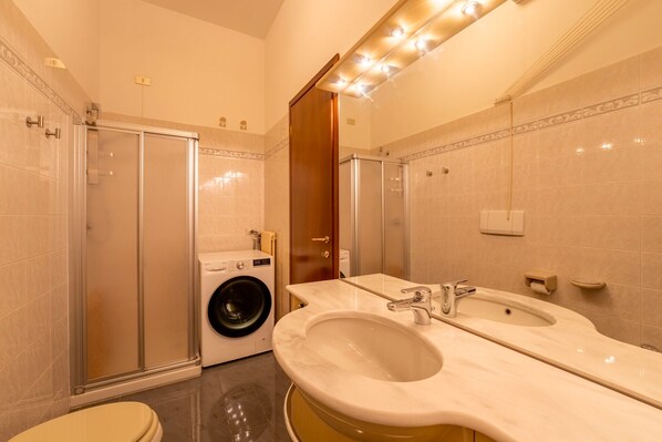 A modern bathroom with a glass shower enclosure, a built-in washing machine, and a double sink vanity. - Varenna Sunset by Wonderful Italy (Varenna)