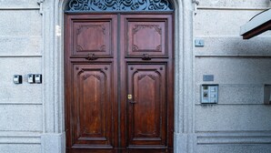 Une grande porte à deux battants en bois, ornée de sculptures complexes, encastrée dans un mur de pierre.