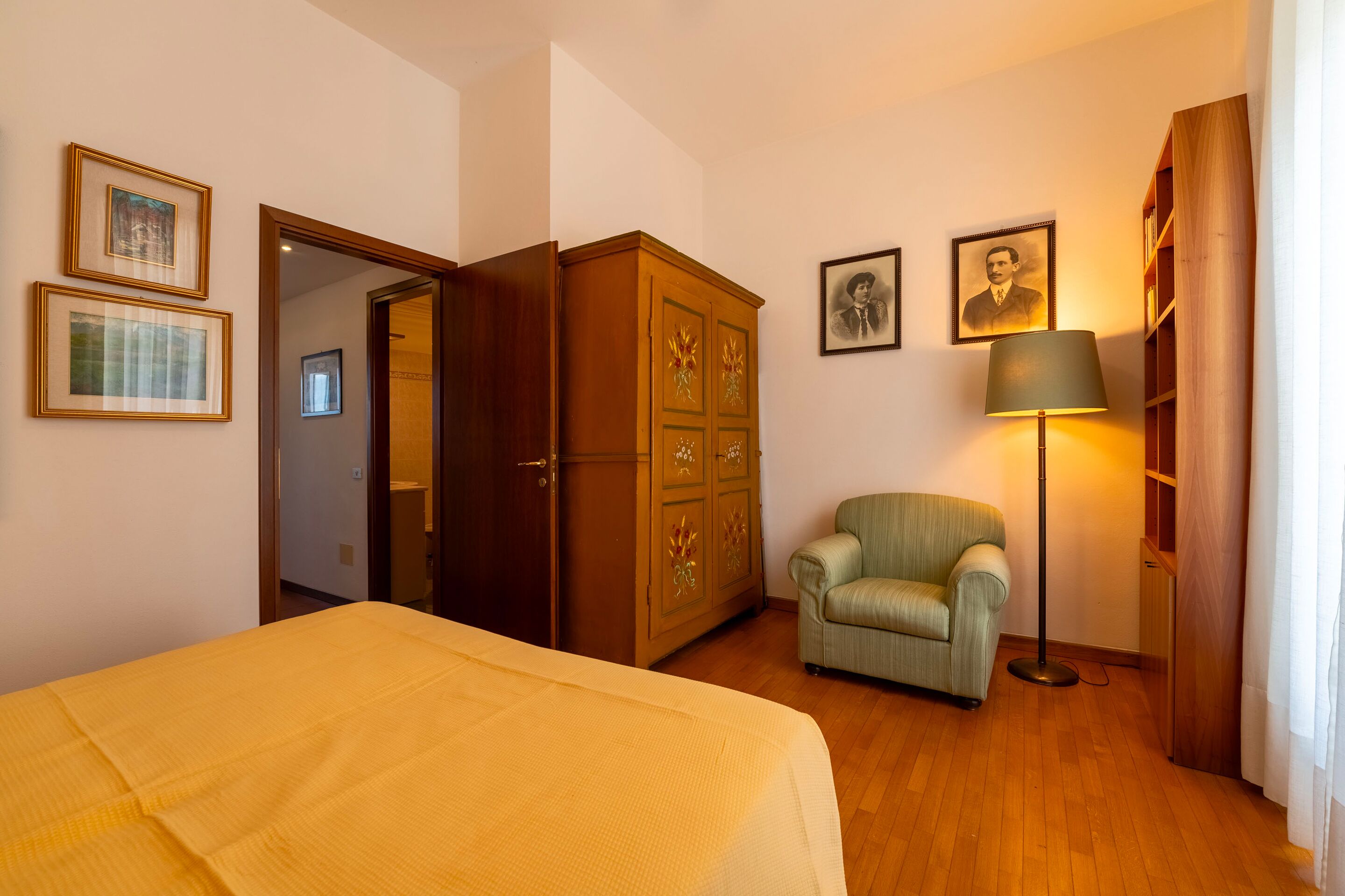 Een kamer met een bed, een groene fauteuil, een houten garderobe en een vloerlamp.