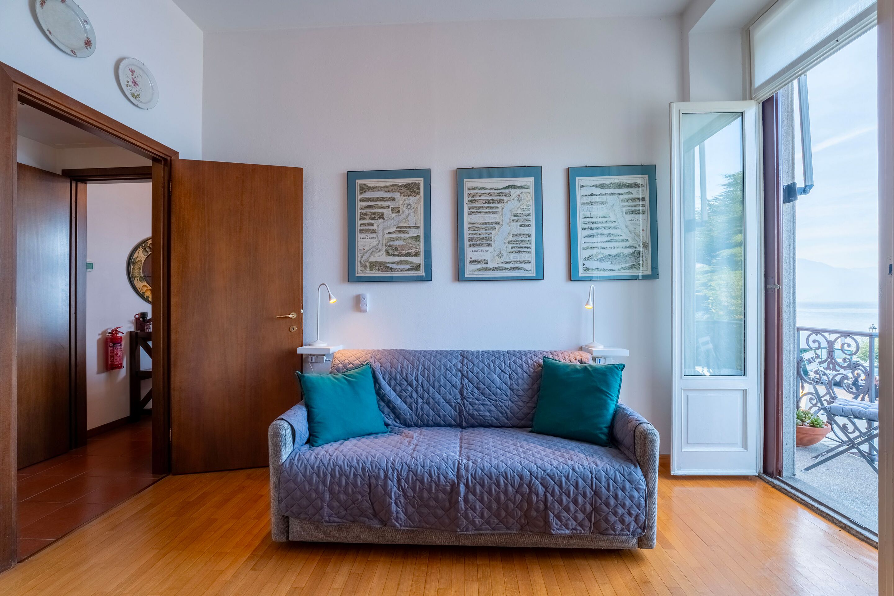 Ein gemütliches Wohnzimmer mit einem grauen gesteppten Sofa, türkisfarbenen Kissen und gerahmten Dokumenten an der Wand.