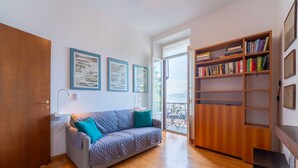 Un salon chaleureux avec un plancher en bois, un canapé gris agrémenté de coussins turquoise, une bibliothèque en bois et des cartes encadrées accrochées au mur.