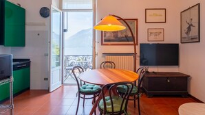 Un coin repas avec une table en bois, des chaises rembourrées de couleur verte, une suspension, un téléviseur et des œuvres d’art accrochées aux murs.