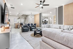 Uma sala de estar moderna com sofá, poltronas, mesa de centro e televisão.