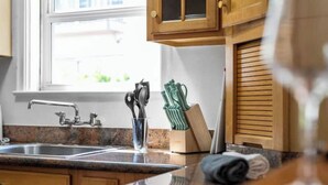 Une cuisine dotée d’un plan de travail en granit, d’un évier en acier inoxydable, de meubles de rangement en bois et d’une fenêtre avec des stores.