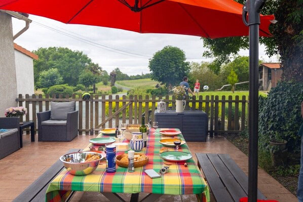 Eine Terrassenanlage im Freien mit Esstisch, umgeben von Korbmöbeln und einem roten Sonnenschirm.