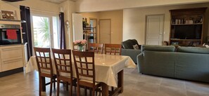 Ein Essbereich mit Tisch und Stühlen, eine Küche mit Ofen, ein grünes Sofa und ein Bücherregal.