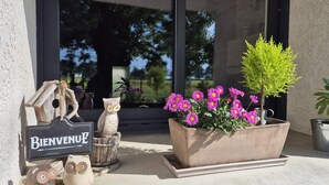 Une pancarte d’accueil, des décorations en forme de hibou, un jardinier avec des fleurs et une plante en pot devant un bâtiment.